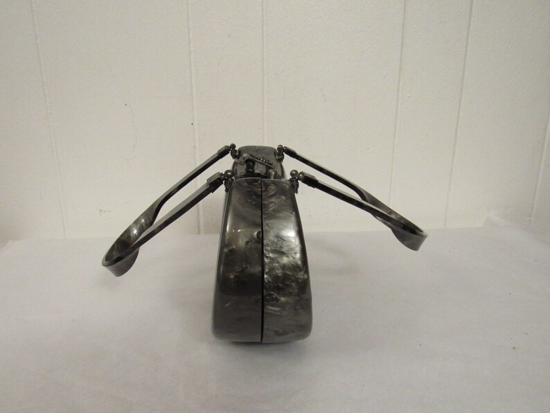 May include: A black and silver clutch purse with a unique design. The purse has two handles that fold out from the sides.