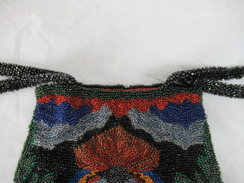 Puede incluir: Un bolso de noche de cuentas con un patr&oacute;n geom&eacute;trico en tonos de verde, azul, rojo y plateado. El bolso tiene una larga correa de cadena de cuentas.