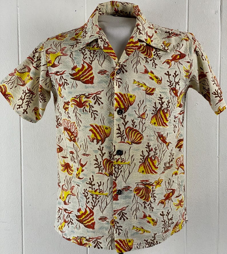 May include: A short-sleeved button-up shirt with a white background and a pattern of red and yellow fish and coral.