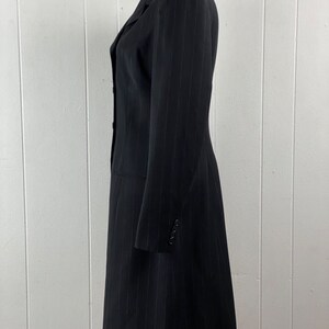 May include: A long black pinstripe blazer with a single button closure and long sleeves.