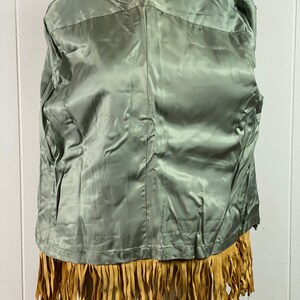 Puede incluir: Una chaqueta de gamuza marr&oacute;n con ribete de flecos. La chaqueta tiene un forro de sat&eacute;n verde.