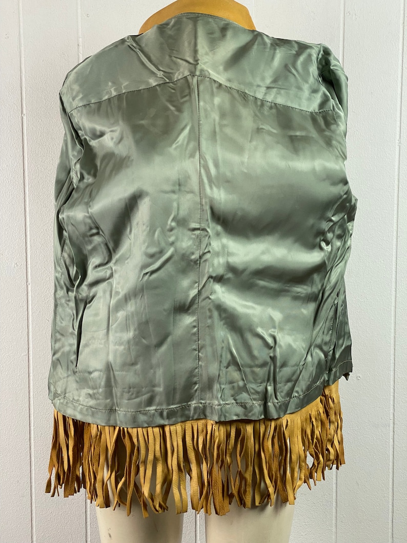 Puede incluir: Una chaqueta de gamuza marr&oacute;n con ribete de flecos. La chaqueta tiene un forro de sat&eacute;n verde.