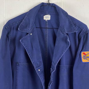 May include: A dark blue work jacket with a zipper closure and a Sunoco logo patch on the right sleeve.