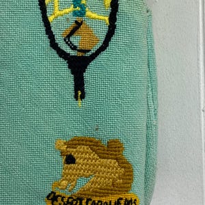 May include: A light blue canvas tote bag with a yellow, green, and black embroidered design of a tennis racket and a horse. The bag also has the text "455RT CABALLEROS" embroidered in yellow and red.