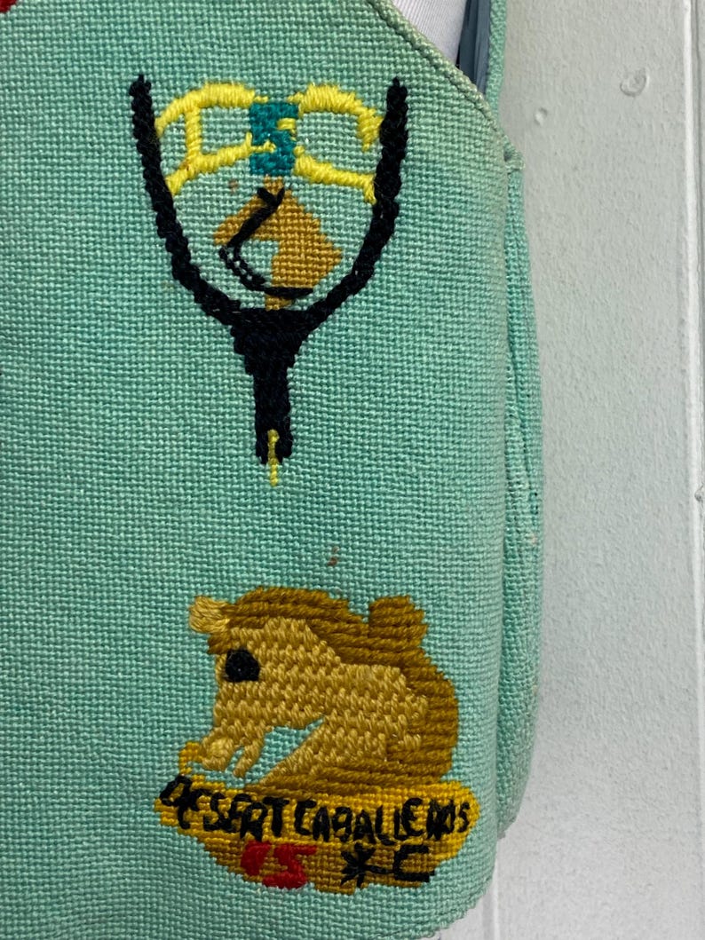 May include: A light blue canvas tote bag with a yellow, green, and black embroidered design of a tennis racket and a horse. The bag also has the text "455RT CABALLEROS" embroidered in yellow and red.