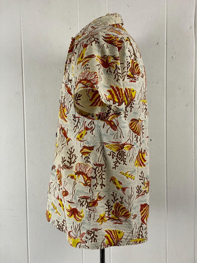 May include: A short-sleeved button-up shirt with a white background and a colorful pattern of red, yellow, and orange fish and coral.