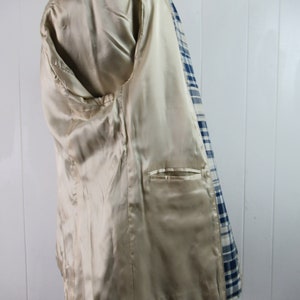 May include: A blue and white plaid blazer with a beige satin lining. The blazer has a single pocket on the inside.