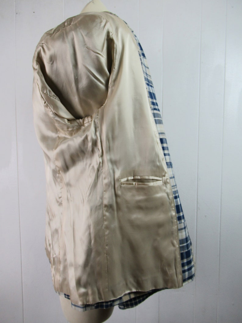 May include: A blue and white plaid blazer with a beige satin lining. The blazer has a single pocket on the inside.