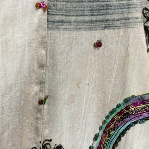 May include: A white linen fabric with a colorful rainbow design and sequins. The fabric has a black and white striped pattern in the upper left corner. There are several sequins in various colors, including pink, green, and gold.