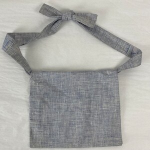 May include: A gray linen crossbody bag with a long strap. The strap has the word "Eve" written on it in blue.