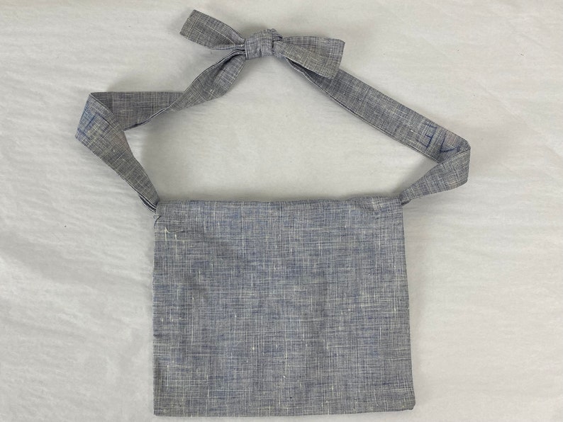 May include: A gray linen crossbody bag with a long strap. The strap has the word "Eve" written on it in blue.