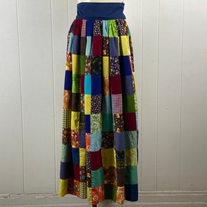 Könnte beinhalten: Ein langer, bunter Patchworkrock mit einem blauen Bund. Der Rock besteht aus verschiedenen Stoffen in den Farben Grün, Gelb, Blau, Rot und Braun.