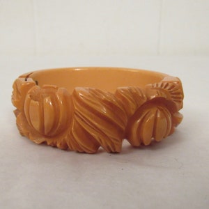 Puede incluir: Un brazalete vintage de baquelita naranja tallado con un dise&ntilde;o floral.