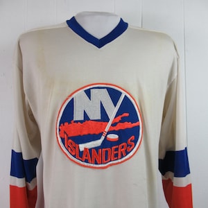May include: A white hockey jersey with the New York Islanders logo. The logo is a blue circle with a white "NY" and a red outline of Long Island. The words "Islanders" are written in white below the circle.