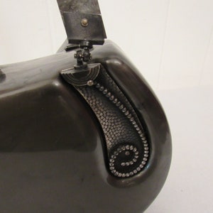 May include: A black metal vintage camera with a silver handle and a silver decorative detail on the side.