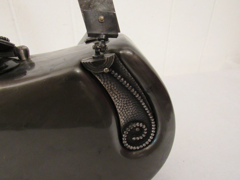 May include: A black metal vintage camera with a silver handle and a silver decorative detail on the side.