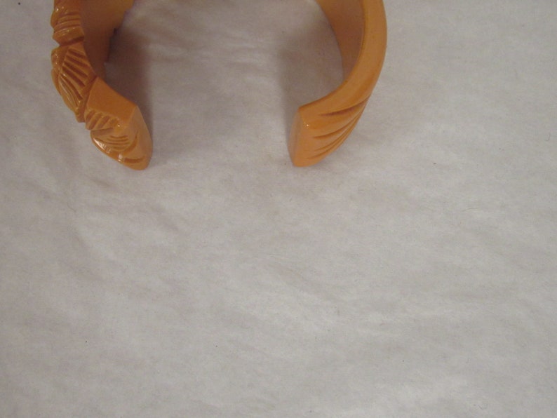 Puede incluir: Un brazalete vintage de pl&aacute;stico naranja con un dise&ntilde;o tallado.