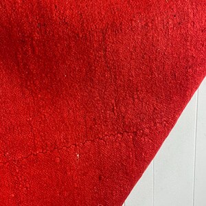 May include: A close-up of a red woven rug with a fringe border. The rug is folded in half and the texture of the fabric is visible.
