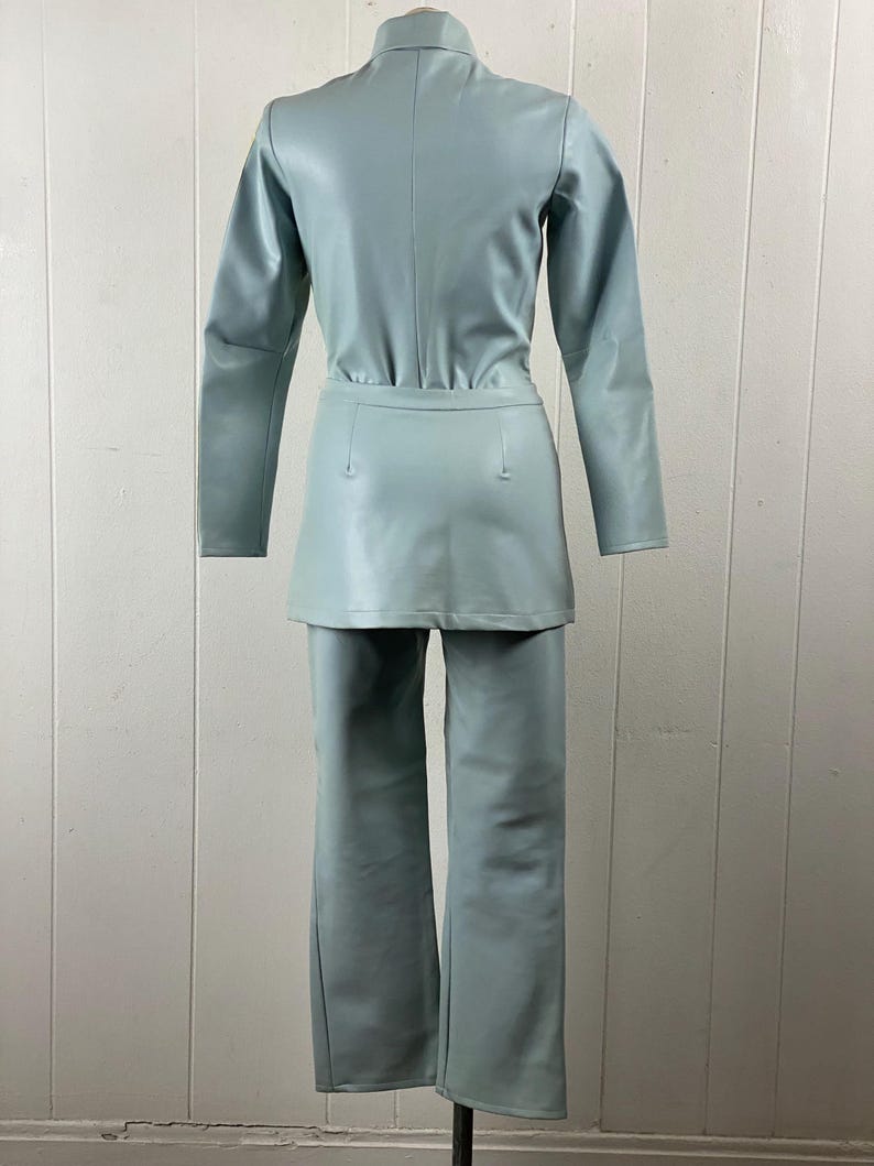 K&ouml;nnte beinhalten: Ein hellblauer Kunstleder-Jumpsuit mit Stehkragen und langen &Auml;rmeln. Der Jumpsuit hat einen Rock und eine Hose.