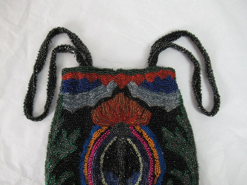 Puede incluir: Un bolso de noche de cuentas con fondo negro y dise&ntilde;os geom&eacute;tricos coloridos. El bolso tiene dos correas de cuentas negras.