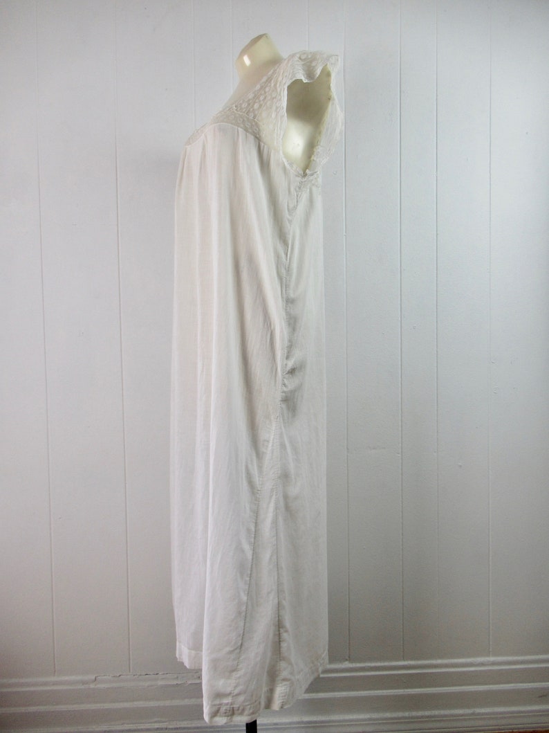 Puede incluir: Un camis&oacute;n blanco de algod&oacute;n con un ribete de encaje alrededor del cuello y las mangas. El camis&oacute;n es largo y fluido, y se muestra en un maniqu&iacute;.