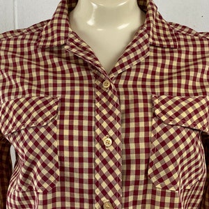 May include: A long-sleeved button-down shirt with a red and cream gingham pattern. The shirt has two chest pockets and a classic collar.