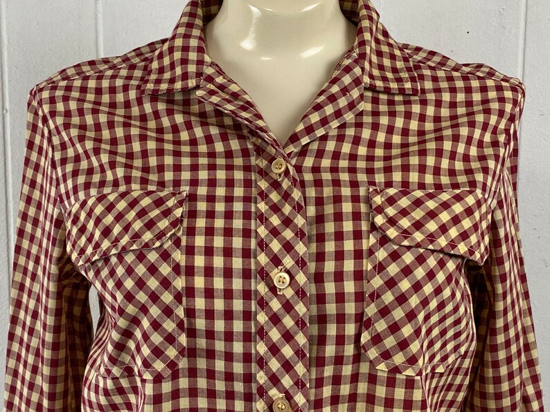 May include: A long-sleeved button-down shirt with a red and cream gingham pattern. The shirt has two chest pockets and a classic collar.