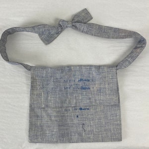 May include: A gray linen bag with a blue embroidered design. The bag has a long strap and a small pocket on the front. The embroidery says "Meet Again" and "Meet Again".