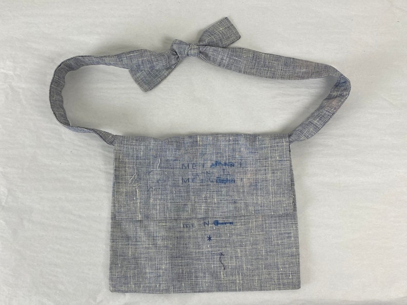 May include: A gray linen bag with a blue embroidered design. The bag has a long strap and a small pocket on the front. The embroidery says "Meet Again" and "Meet Again".