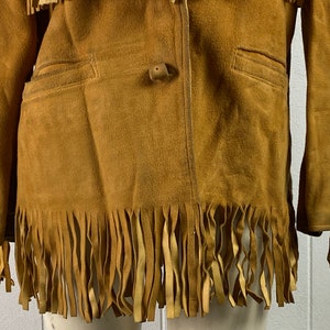 Puede incluir: Una chaqueta de ante marr&oacute;n con detalles de flecos en las mangas y el dobladillo inferior. La chaqueta tiene un cierre de bot&oacute;n &uacute;nico y dos bolsillos.