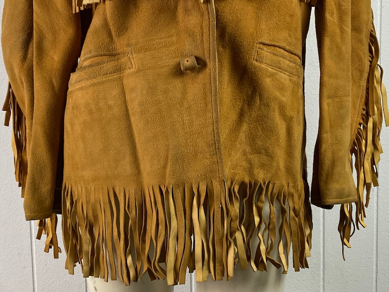 Puede incluir: Una chaqueta de ante marr&oacute;n con detalles de flecos en las mangas y el dobladillo inferior. La chaqueta tiene un cierre de bot&oacute;n &uacute;nico y dos bolsillos.