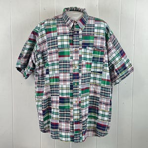 May include: A short-sleeve button-down shirt featuring a multi-colored patchwork plaid pattern in shades of green, red, blue, and white. The shirt includes a standard collar, a front button placket, and a single chest pocket on the left side.
