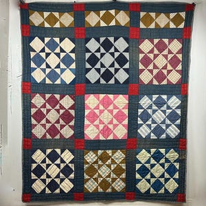 May include: A rectangular quilt featuring a grid of nine square blocks, each composed of smaller triangles in various patterns and colors including blue, pink, brown, and white. The blocks are separated by dark blue sashing and red corner squares.