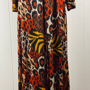 Puede incluir: Un vestido largo de manga larga con cierre de botones en la parte delantera y un estampado de animales colorido. El estampado presenta una mezcla de leopardo, cebra y rayas de tigre en tonos naranja, marr&oacute;n, negro y blanco.