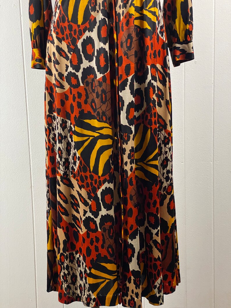 Puede incluir: Un vestido largo de manga larga con cierre de botones en la parte delantera y un estampado de animales colorido. El estampado presenta una mezcla de leopardo, cebra y rayas de tigre en tonos naranja, marr&oacute;n, negro y blanco.