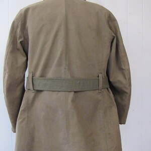 May include: A tan-colored jacket with a brown corduroy collar and a green canvas belt. The jacket has a long, straight cut and a single-breasted closure.