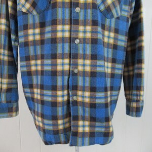 以下が含まれることがあります： 長袖でボタン留めの青い、茶色、黄色の格子柄のフランネルシャツです。