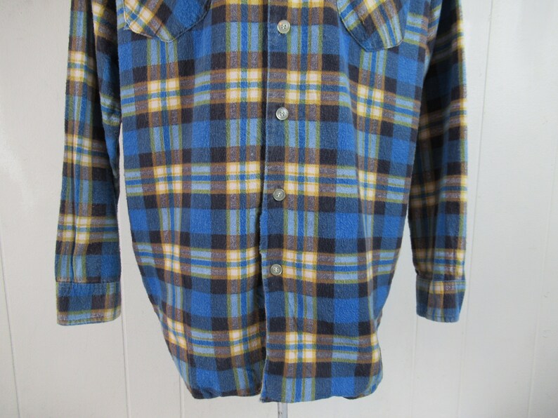以下が含まれることがあります： 長袖でボタン留めの青い、茶色、黄色の格子柄のフランネルシャツです。