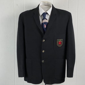 May include: A black blazer with a gold button closure and a patch on the left pocket. The patch features a red and green crest with a gold outline.