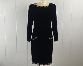 Könnte beinhalten: Schwarzes Samtkleid mit goldenen Verzierungen an Ausschnitt und Taschen. Das Kleid hat lange Ärmel und eine figurbetonte Silhouette.