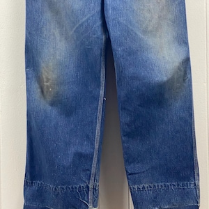 K&ouml;nnte beinhalten: Nahaufnahme einer Vintage-Jeans aus blauem Denim. Die Jeans hat eine verblasste Waschung mit Gebrauchsspuren und ein weites Bein. Die S&auml;ume sind umgeschlagen und mit wei&szlig;em Faden gen&auml;ht. Der Denim hat einen klassischen, strapazierf&auml;higen Look.