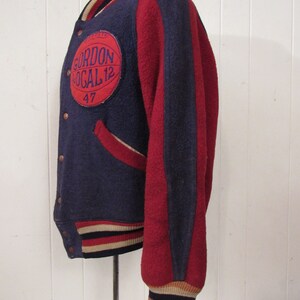May include: A vintage blue and red varsity jacket with a white and black striped cuff. The jacket has a large circular patch on the left chest with the text "Gordon Local 12" and the number "47" underneath.