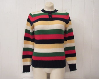 Può includere: Un maglione a righe con maniche lunghe e colletto abbottonato. Il maglione è realizzato in un tessuto morbido e lavorato a maglia e presenta una varietà di colori, tra cui rosso, verde, blu, bianco e giallo.