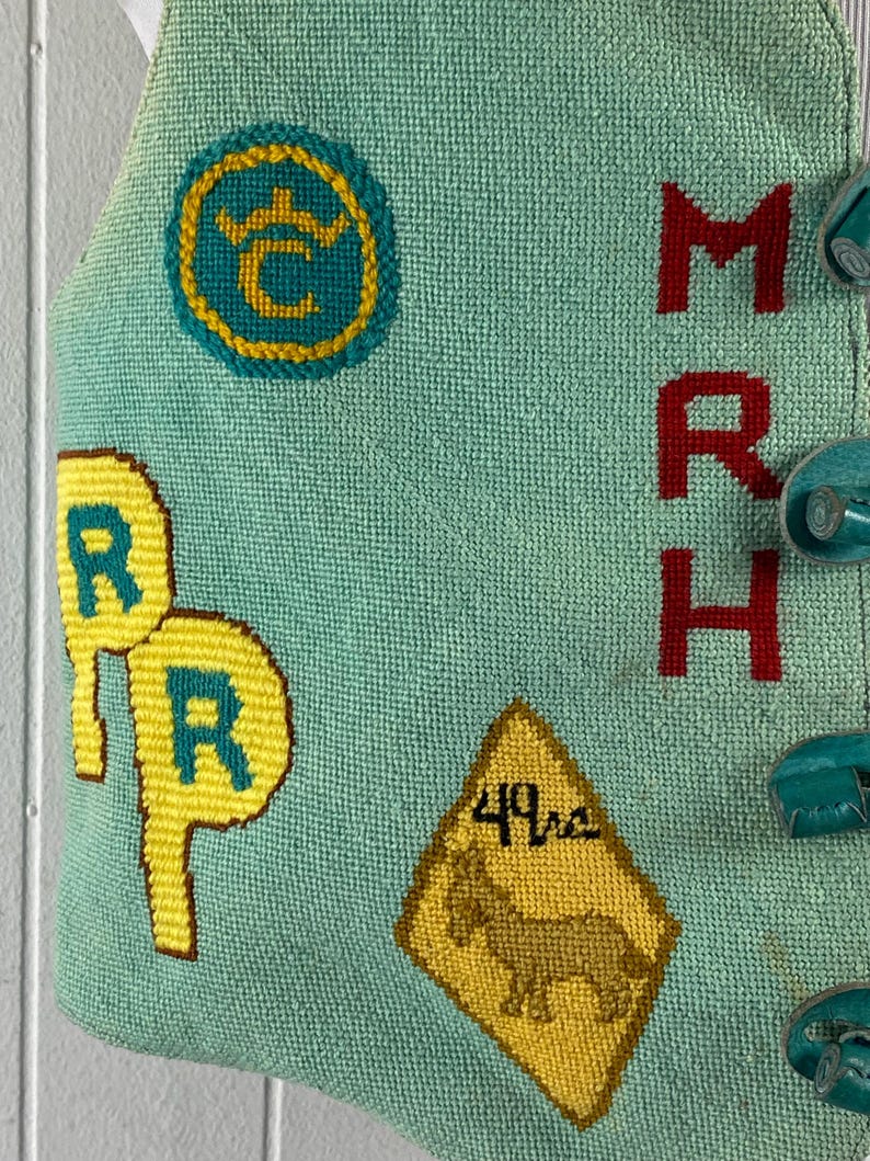 May include: A turquoise blue fabric with embroidered details. The fabric features a yellow circle with a crown and the letter "C" inside, two yellow circles with the letter "R" inside, a yellow diamond-shaped sign with the text "49ers" and a brown horse inside, and the letters "MRH" in red.