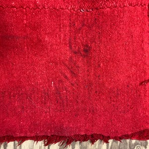 May include: A close-up of a red fabric with a fringed edge. The fabric has a textured surface and appears to be worn.