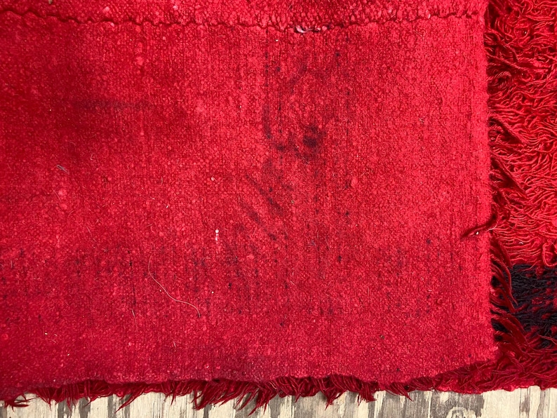 May include: A close-up of a red fabric with a fringed edge. The fabric has a textured surface and appears to be worn.