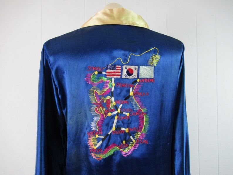 May include: A blue satin robe with an embroidered map of South Korea on the back. The map includes the names of cities and the flags of the United States and South Korea.