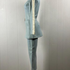 K&ouml;nnte beinhalten: Ein hellblauer Jumpsuit mit einem wei&szlig;en Streifen an der Seite jedes &Auml;rmels. Der Jumpsuit hat einen Rei&szlig;verschluss und einen G&uuml;rtel.