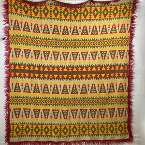 May include: A red, yellow, and green patterned throw blanket with a fringe border. The blanket features a geometric design with triangles, diamonds, and zigzags.