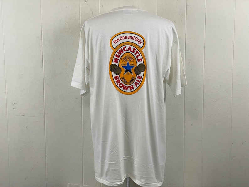 May include: White t-shirt with a Newcastle Brown Ale logo on the back. The logo is circular with the words "The One and Only" at the top, and "Newcastle Brown Ale" at the bottom. The logo features a blue star.